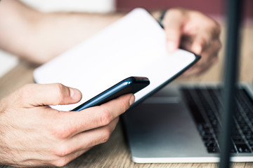 close-up partial view of person holding notebook and using smartphone