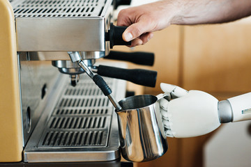 close-up view of robotic arm and human hand preparing coffee in coffee machine
