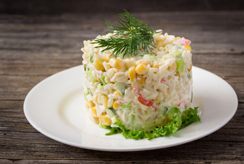 Fresh vegetable salad with corn, pepper, crab, cucumber, eggs and mayonnaise on the plate.