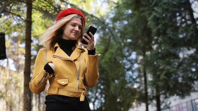 successful caucasian woman with smart phone outdoors in green park enjoying spring weather young blonde female person in red hat using cellphone on sunny day smiling cheerful face online chatting
