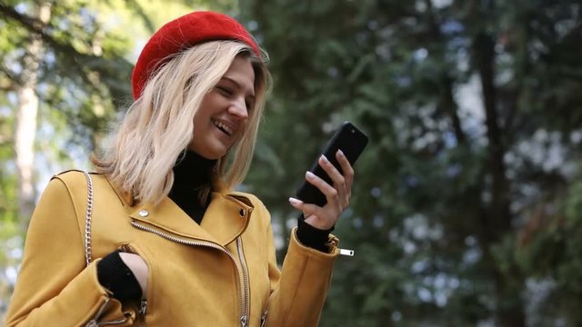 laughing caucasian woman using smart phone outdoors in park enjoying warm weather blonde female person in red hat networking online urban lifestyle cellphone sunny day smiling face online chatting