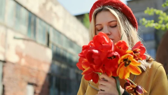 young successful business woman enjoying sunny day holding red tulips bouquet on street then smelling flowers and closing eyes pretty lady fashionable look modern urban lifestyle peaceful mood