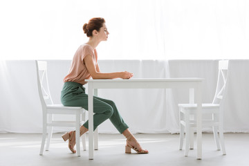 side view of attractive young woman sitting at table alone at home - Powered by Adobe
