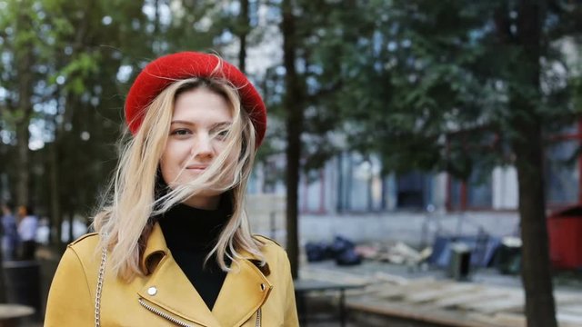 ashion stylish portrait of pretty young hipster blonde woman standing outside looking at camera calm face elegant red hat beret jacket bright colors cool girl green summer sunny nature on background