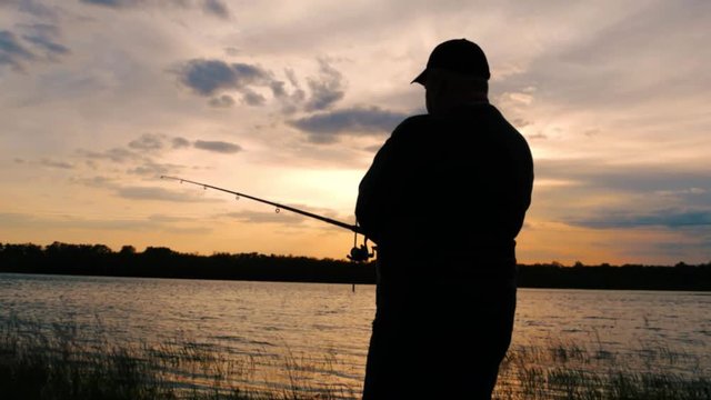 Silhouette fisherman throwing fishing rod in river on background evening sunset. Beautiful evening sunset during fishing on river. Sport hobby fishing.