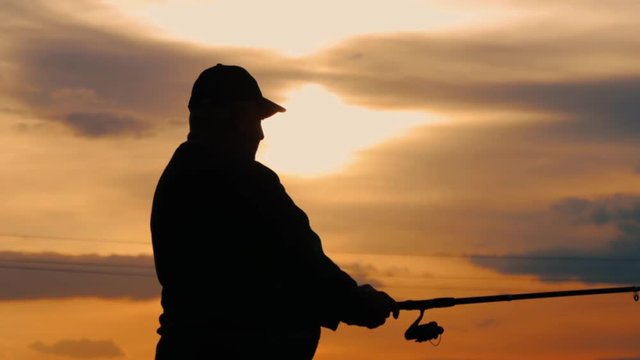 Silhouette fisherman throwing fishing rod in river on background evening sunset. Beautiful evening sunset during fishing on river. Sport hobby fishing.