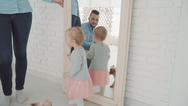 Beautiful little girl stay near the mirror with her family and dog. Slow Motion. Baby milestone, toddler, 1 year old. Happy childhood