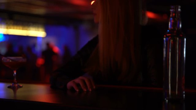 Woman waiting for ordered cocktail at bar counter, drumming fingers impatiently