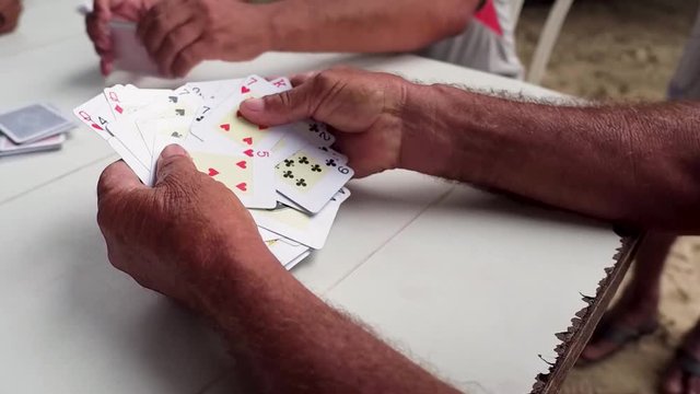 A group of elderly friends finish a game of cards and begin to shuffle them back into a deck