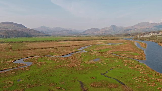Aerial view of the Glaslyn Marshes close to the railway with the Snowdonia mountain range national park in background - Porthmadog, Wales - United Kingdom