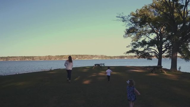 An Aerial Chase of a Young Mother and Her 2 Children Running and Playing at the Lake