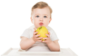 Fototapeta premium baby boy holding apple and sitting in highchair isolated on white background