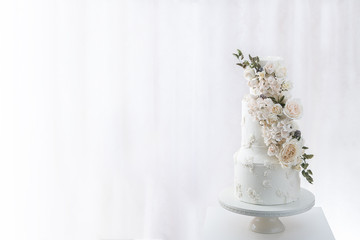 White tiered wedding cake with edible bouquet of flowers wrapped around it. (Left)