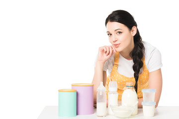 smiling young woman in apron at table with children food and milk isolated on white background