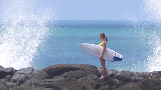 SLOW MOTION, COPY SPACE: Powerful waves hit the remote beach while surfer girl enjoys the spectacular view of the ocean. Lonely young woman looks around the breathtaking black shore in New Zealand.