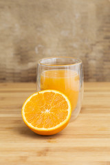 Orange juice served on a transparent glass with a half slice orange on a wooden table background