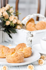 Many tasty cakes of Shue from custard paste with cream stuffing lie on a round plate on a white wooden table.