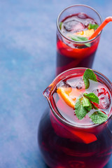 Refreshing Non-Alcoholic Spanish Sangria from Variety of Fruits Orange Citrus Pomegranate Grapes Berries and Fresh Mint in Pitcher and Tall Glass on Blue Background. Summer Detox Superfoods Concept
