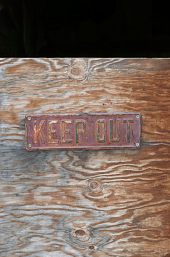 Metal sign with the words "Keep out" on a wooden background