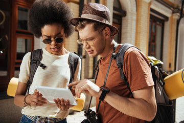 Obraz premium serious multicultural couple of tourists with digital tablet looking for destination