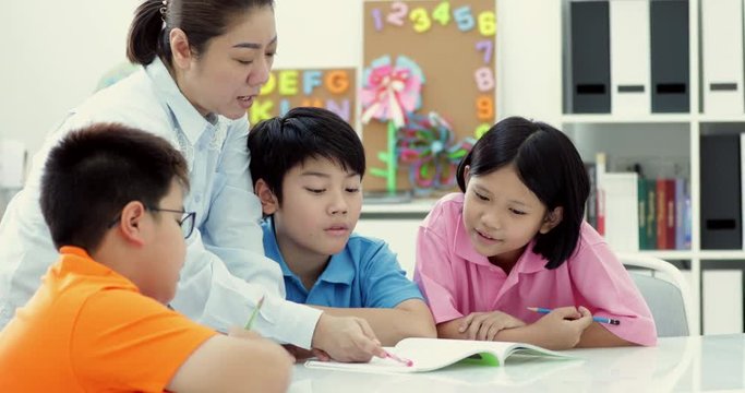 Young asian teacher helps young school kids in class, close up