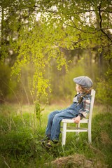 Naklejka na ściany i meble Young blonde boy relaxing on white old chair in spring landscape