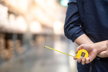 close up of male hand holding yellow tape measure in warehouse. Furniture product design measuring concept