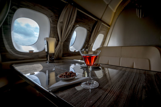 Interior of a business class of a commercial passenger plane, an armchair and a window, a table and a cocktail glass with a drink.