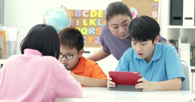 Asian teacher and Three kids entertaining themselves using digital tab and laughing