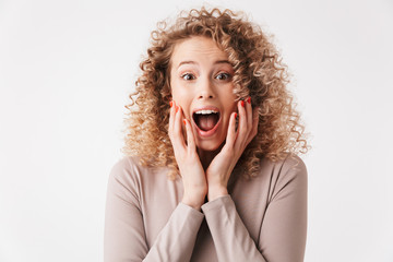 Surprised happy blonde curly woman in dress touching her cheeks