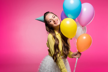 attractive woman posing with party hat and balloons isolated on pink