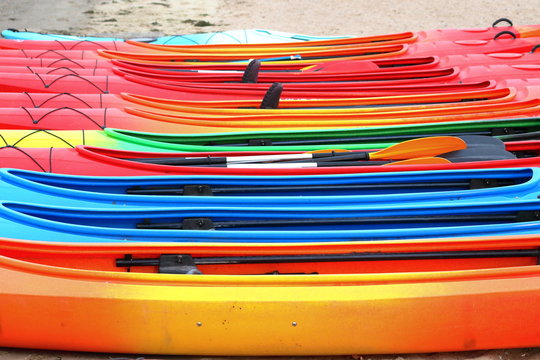 Many bright colored kayaks on sand shore at autumn cloudy day