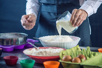 Chef pastry in a black apron in the process of making cupcakes from ingredients. Concept of confectionery cooking