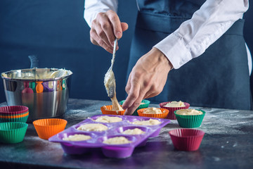 Chef pastry in a black apron filling the dough into a cupcake silicone mold. Concept of...