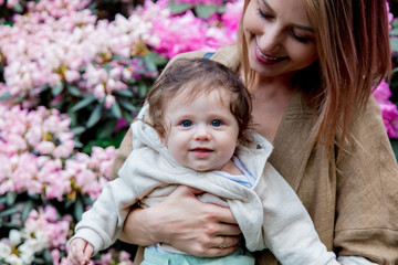 Young mother holding a male baby near a blossom flowers in park. Spring time season