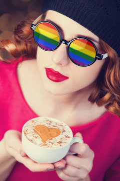 Redhead girl in glasses with rainwob sunglasses and with cup of coffee.