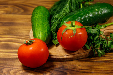Fresh tomatoes, cucumbers, parsley and dill on cutting board on wooden table