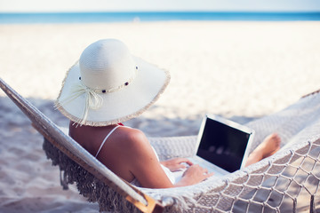 Woman using her laptop in hammock on the beach
