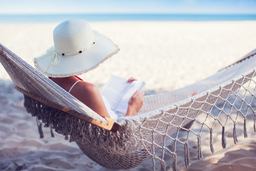 Young lady reading a book in hammock on tropical sandy beach