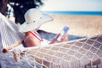 Young lady reading a book in hammock on tropical sandy beach