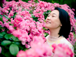 Fototapeta premium Outdoor portrait of beautiful young Chinese woman in yellow dress smiling among pink rose flowers wall in spring garden.