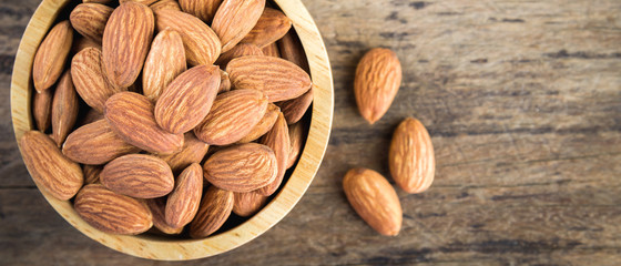 Almonds in brown bowl on textured wooden background.