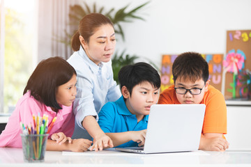 Teacher and Cute Asian children using laptop computer together.