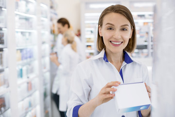 Responsible employee. Merry female pharmacist smiling to camera and holding drug