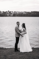 An amazing couple on their wedding day near the lake hug and enjoy each other. The bride and groom with a bouquet are happy together