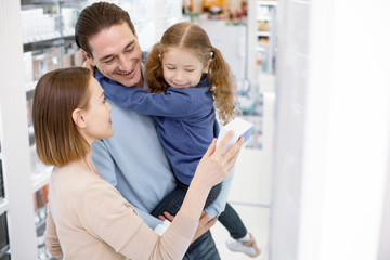 Local drugstore. Jovial jolly woman selecting drug while man holding girl