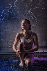 Girl in the white shirt with water drop in a dark room illuminated by light during a photoshoot with water