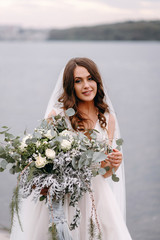 An amazing bride in a beautiful wedding dress on her wedding day walks by the lake. Portrait of a...