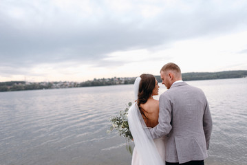 An amazing couple on their wedding day near the lake hug and enjoy each other. The bride and groom...