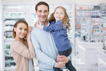 Together in drugstore. Enthusiastic adorable family coming in drugstore and grinning to camera